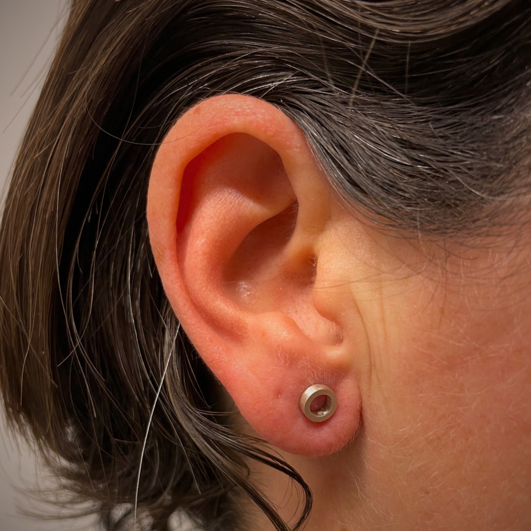 Close up of a woman’s ear who is wearing a sterling silver earring with a circular shape that has a diameter of 6 mm.